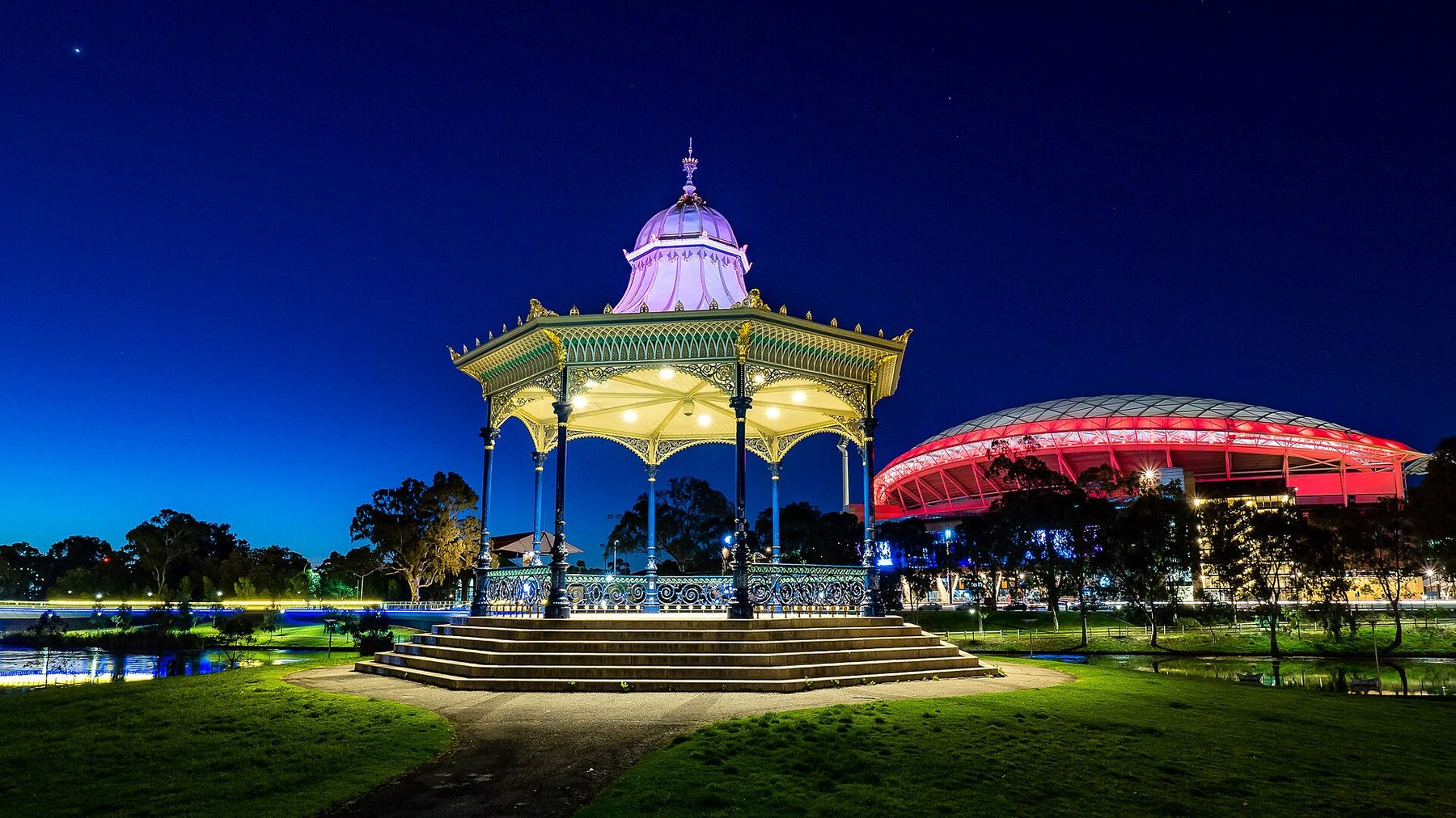 The historic Elder Park rotunda lit up at blue hour, with Adelaide Oval in the background